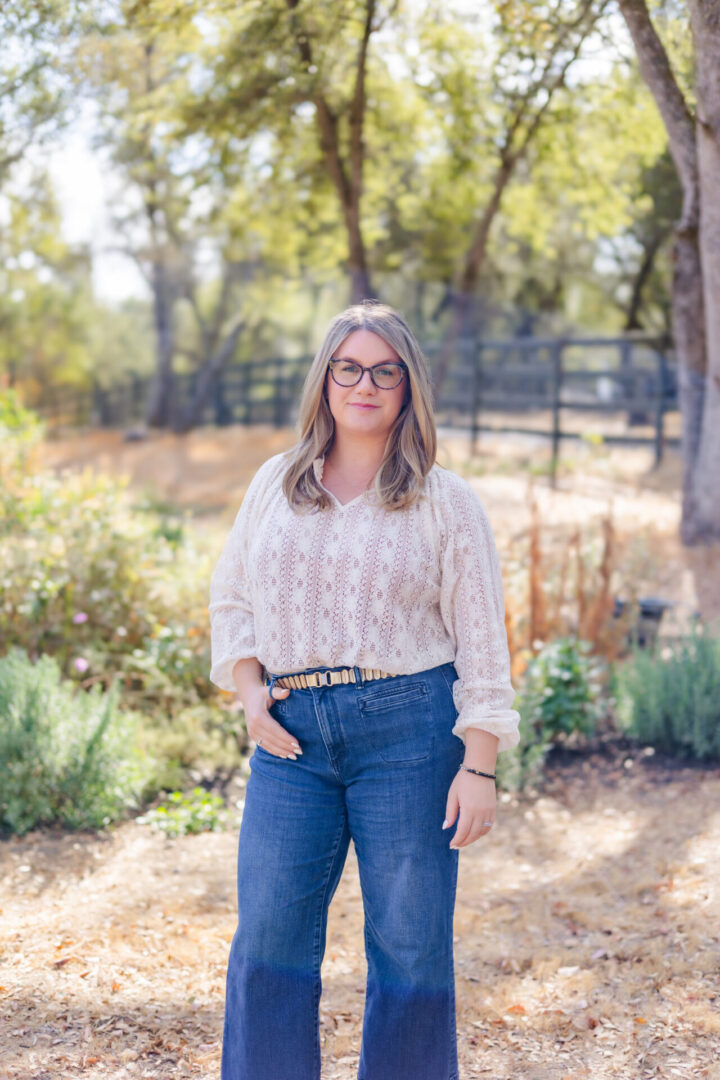 A woman standing in the dirt wearing jeans and a white shirt.