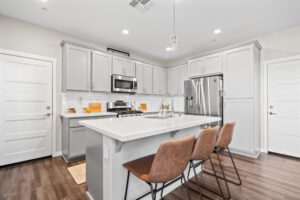 A kitchen with white cabinets and brown chairs.